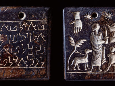 Two images of a rectangular plaque: one side shows an inscription in a Semitic script, and the other depicts a person with a knife, a child, a four-legged animal, two stars, and a hand reaching down from the sky. There is a hole in the top center of the plaque.