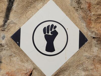Photograph of a white diamond-shaped tile, affixed to a stone surface, depicting a black fist in a circle
