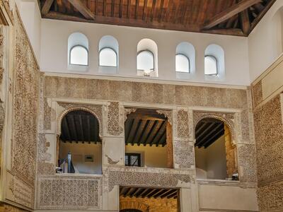 Interior of a large room with windows, with intricate geometric patterns and Hebrew inscriptions on the walls.