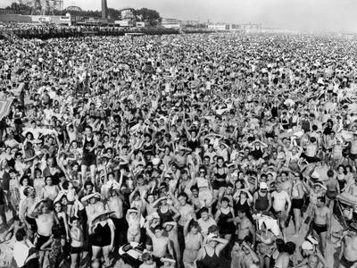 Aerial photograph of hundreds of people crowded together on beach with amusement park in background.