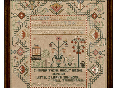 Needlework in a frame with a border of designs, the alphabet and numbers in the center, and text at the bottom.