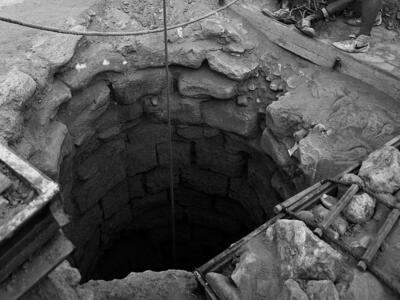 Photograph of stone well with rope system and two figures standing on the side. 