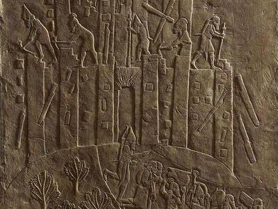 Relief of building with figures on top and below carrying objects. 