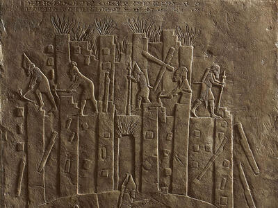Relief of building with figures on top and below carrying objects. 