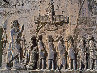 Behistun Trilingual Inscription and Aramaic Papyrus Relief with figures with hands bound standing next to larger figure along wall with relief of winged figure and Persian, Elamite, and Akkadian inscriptions.