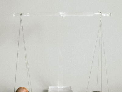 Reconstructed scale with two ancient bronze pans suspended from central beam of clear modern material. The left pan holds a balance weight and the right holds a piece of silver.
