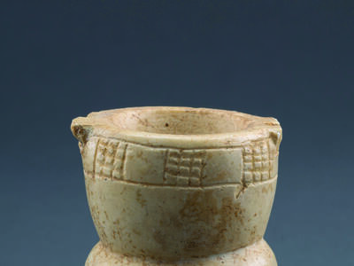 Limestone, goblet-shaped container with a footed base, a midsection with festoon pattern, and a deep bowl with checkerboard pattern on rim.