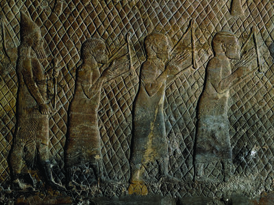 Wall relief showing three bare-headed musicians in tunics holding stringed instruments against their chests, with bearded soldier holding weapon behind them.