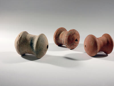 Three spool-shaped terra-cotta objects with a hole on one end.