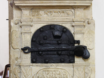 Carved wall unit with decorative borders and crowns, locked metal box in middle, and Hebrew text underneath. 