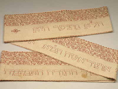 Rectangular cloth, folded in two places, with Hebrew text embroidered on bottom half of cloth and floral border on top half. 