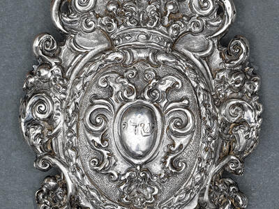 Silver amulet with decorative edges and Hebrew word etched in center. 