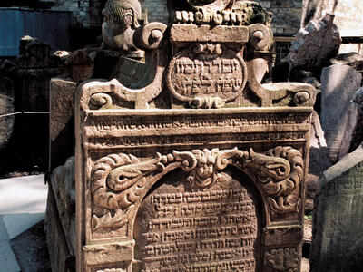 Tomb with high tombstones on either end, lions, shield and floral decorations on top, and Hebrew inscription on surface of stone.