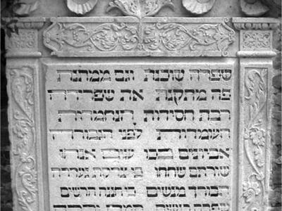 Tombstone of decorative foliage surrounding Hebrew inscription.