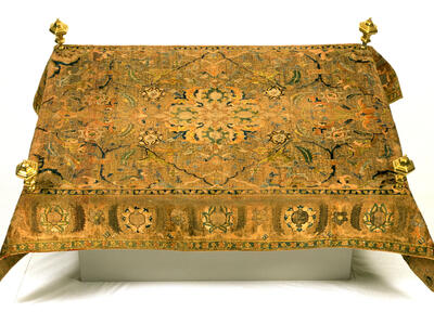 Carpet with embroidered designs and four small posts near each corner. 