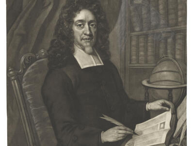 Portrait of a bearded man seated at desk wearing a wig and collar, holding a quill in his right hand and turning the page of book with his left hand, with bookshelf in background and globe and inkwell on desk. 