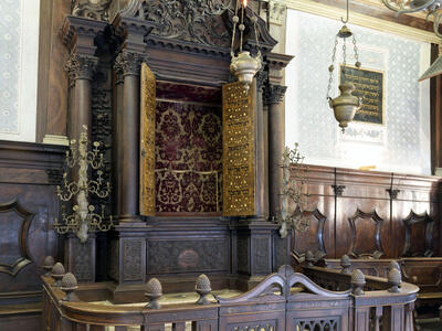 Photograph of carved Torah ark with gold doors, crown at top, and wooden fence around it.