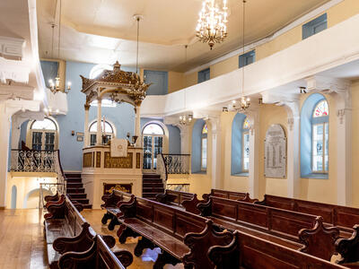 Photograph of room with high ceiling, tall podium up short staircase with golden canopy, and rows of wooden benches. 