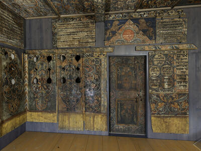Photograph of room with wood walls painted with Hebrew text, animals, and floral designs.