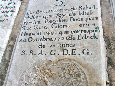 Tombstone with inscription in Hebrew and Portuguese above floral motifs and engraving of hand with an ax reaching out of cloud to chop down tree.