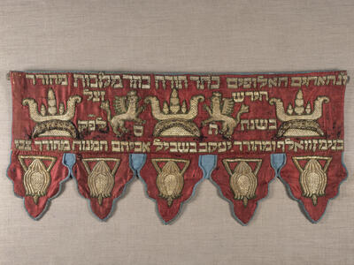 Short curtain embroidered with Hebrew text across the top with griffins and crowns. 