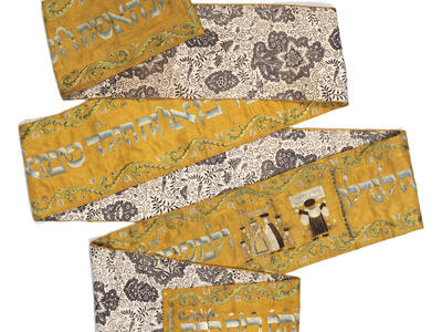 Long rectangular cloth folded in several places, with floral design on one side and Hebrew text on the other side, with image of person reading from the Torah and couple under a wedding canopy. 