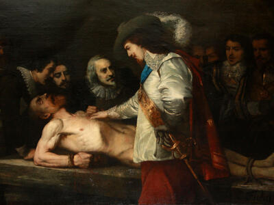 Painting of well-dressed man in hat with plume and sword putting his hand on the chest of a nude man tied down prone on a table with face upturned and mouth open, as several well-dressed men look on from the far side of the table. 