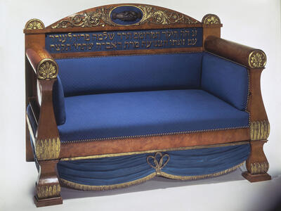 Wooden sofa with upholstered seat, featuring an image of clasped hands and Hebrew inscription on seat back. 