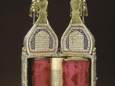 Ornately decorated cylindrical case with Hebrew writing on top and scroll inside; closed cylindrical case with ornate decoration.