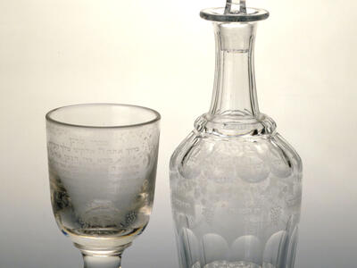 Glass cup and carafe with designs and Hebrew text etched on the outside.