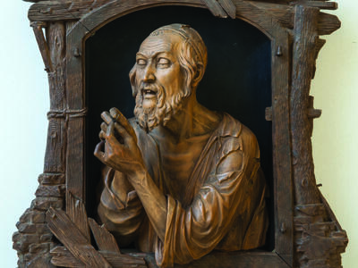 Wood-carving of a man in skullcap examining an object in his hands.
