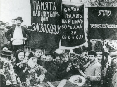 Photograph of crowd of people holding banners in Russian and Yiddish above a coffin.
