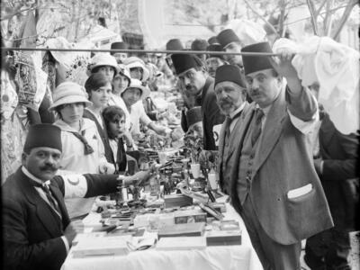 Photograph of women and men in fez hats sitting and standing at a long set table.