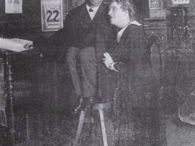 Photograph of two figures looking at each other, one crouched on a stool and the other standing.