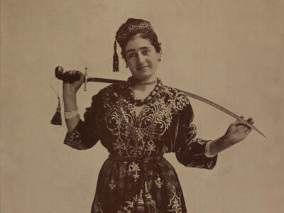 Photograph of figure holding sword behind her neck.