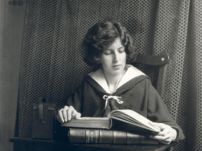 Photograph of figure seated at desk reading a book.