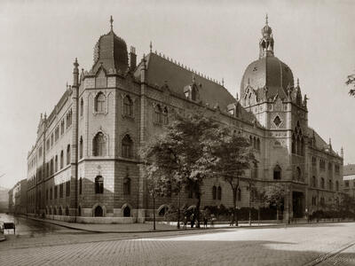 Photograph of brick building on street corner with ornate roof finials and domed roofs.
