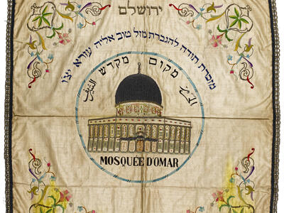 Embroided cloth with domed building in center, surrounded by Hebrew and Arabic text, and flowers in each corner.