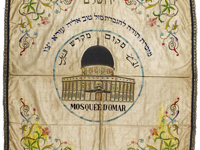 Embroided cloth with domed building in center, surrounded by Hebrew and Arabic text, and flowers in each corner.