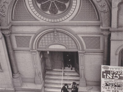 Photograph of building entrance with rose-shaped window and Hebrew inscription seen from above.
