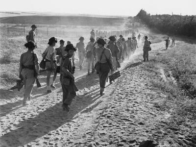 Photograph of troops marching away from the viewer on a sandy trail.