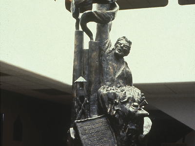 Photograph of sculpture in an atrium depicting man in labor camp with arm raised holding a flag. 