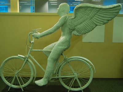 Sculpture of winged figure on bicycle.
