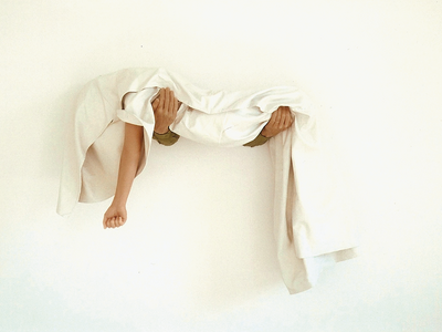 Art installation of arms coming out of a wall holding body covered in sheet with one arm exposed. 