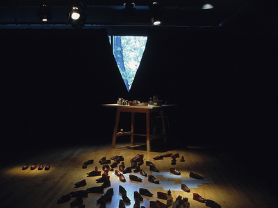 Installation featuring various objects, shoes, and papers on floor. 