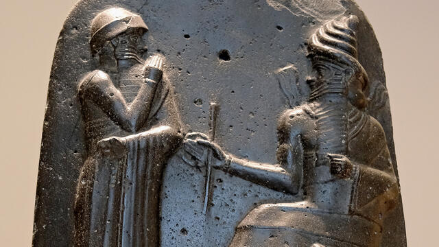 The top of Hammurabi's Stela; Hammurabi stands with a hand to his nose in submission to the seated god Shamash.