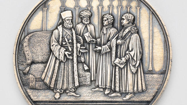 Silver medal depicting four men talking.