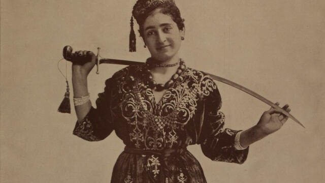 Photograph of figure holding sword behind her neck.